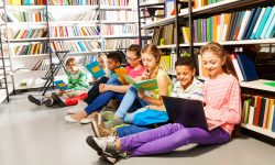 Children sitting on the floor in library and studying holding books